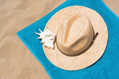 Soft blue beach towel with straw hat and seashell on sand, flat lay