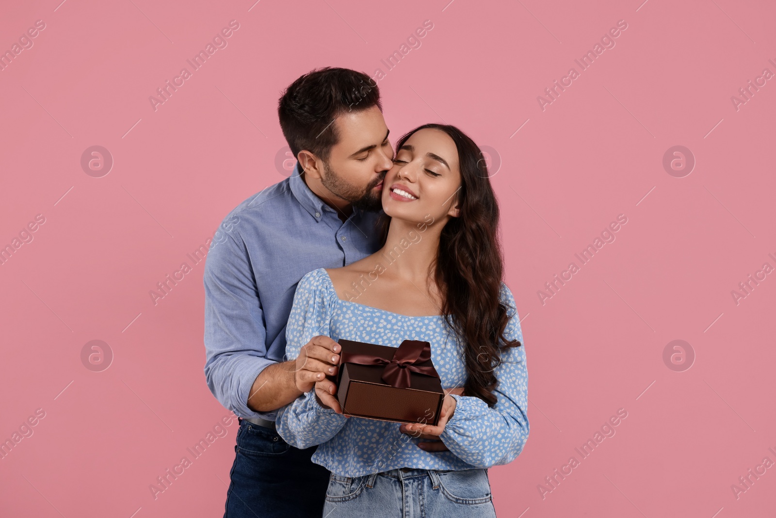 Photo of Man kissing his smiling girlfriend on pink background. Celebrating holiday