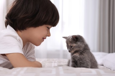Photo of Cute little boy with kitten on bed at home. Childhood pet