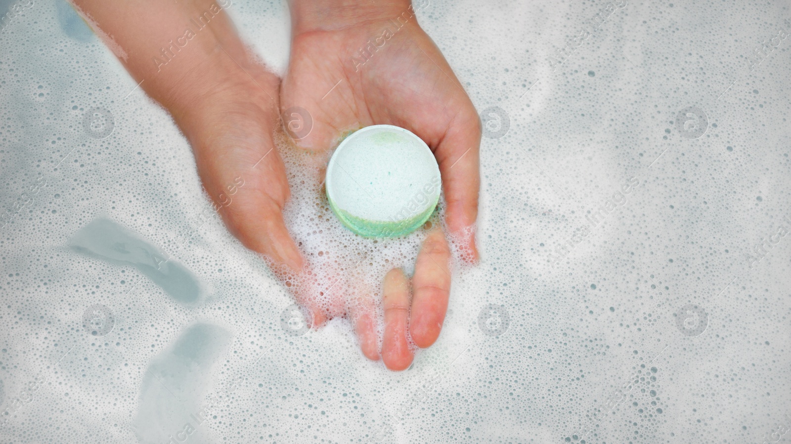 Photo of Woman holding bath bomb over water with foam, top view. Space for text