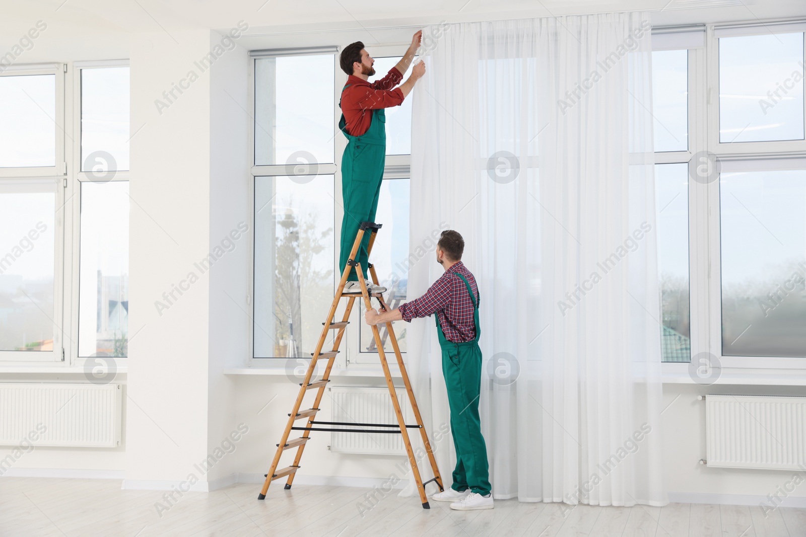 Photo of Workers in uniform hanging window curtain indoors