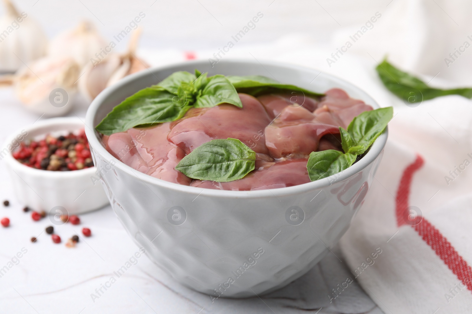 Photo of Bowl with raw chicken liver and basil on white textured table
