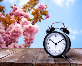 Image of Black alarm clock on wooden table, space for text. Daylight saving time (Spring forward)