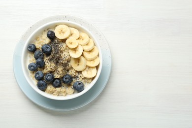 Tasty oatmeal with banana, blueberries and chia seeds served in bowl on white wooden table, top view. Space for text