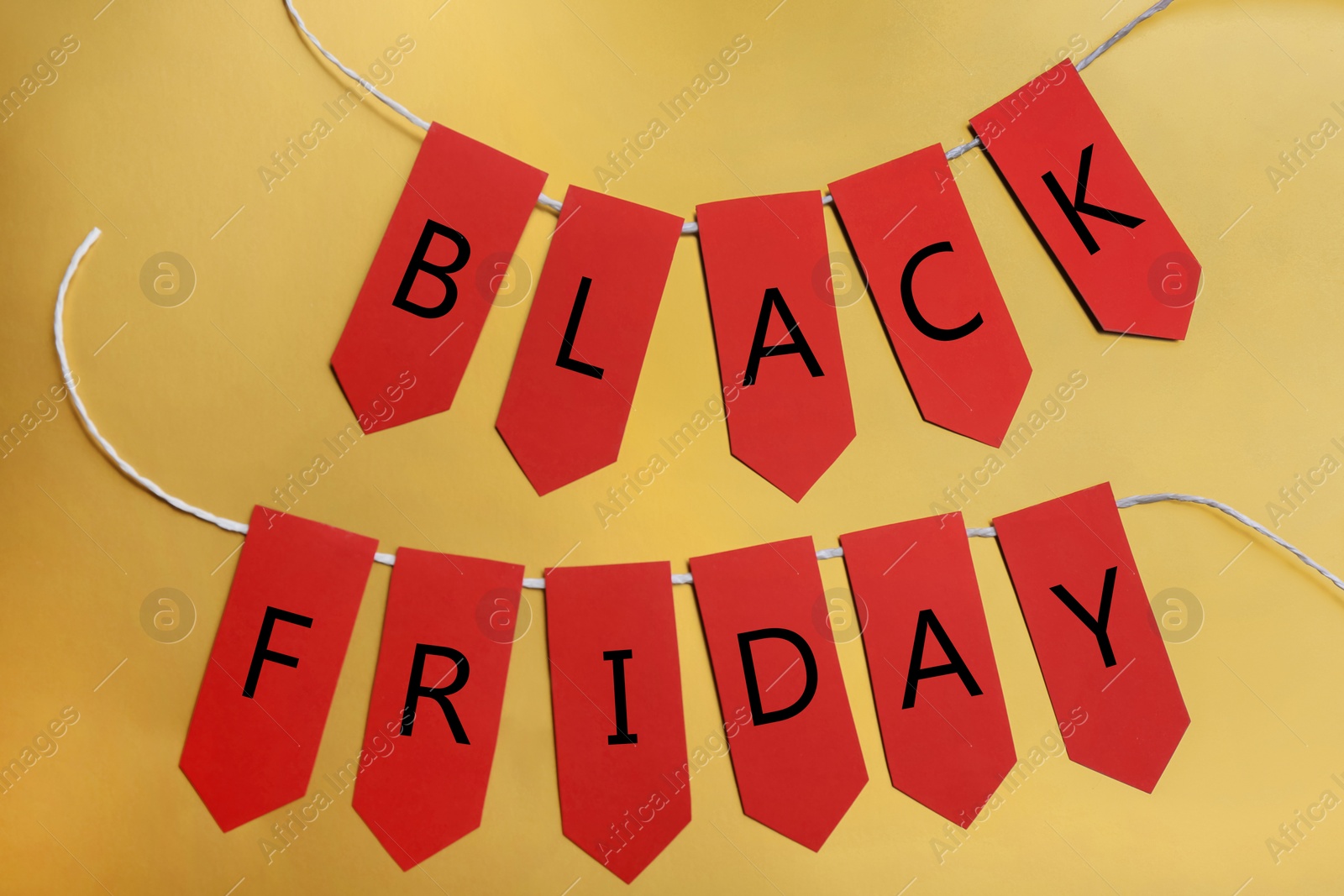 Photo of Words BLACK FRIDAY made with red tags on golden background, flat lay