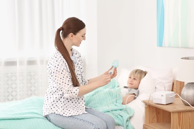 Mother holding nebulizer for inhalation and her son lying on bed at home