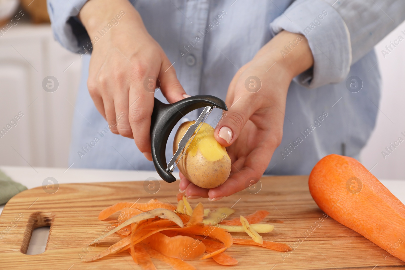 Photo of Woman peeling fresh potato at table indoors, closeup