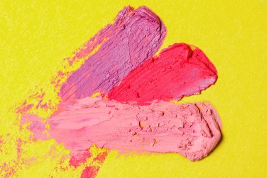Smears of different beautiful lipsticks on yellow background, top view