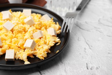 Plate with delicious scrambled eggs and tofu on white textured table, closeup. Space for text