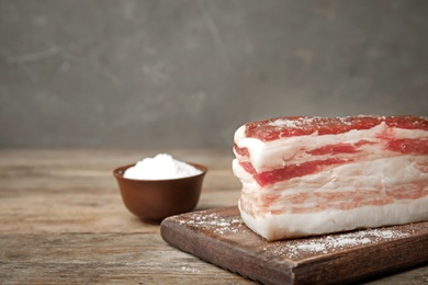 Photo of Board with bacon and salt on wooden table. Space for text