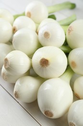 Whole green spring onions on white wooden table, closeup