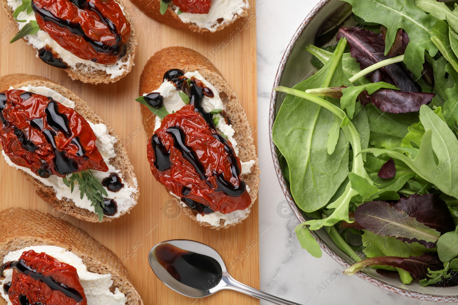 Photo of Delicious bruschettas with sun-dried tomatoes, cream cheese, balsamic vinegar and ingredients on white table, flat lay