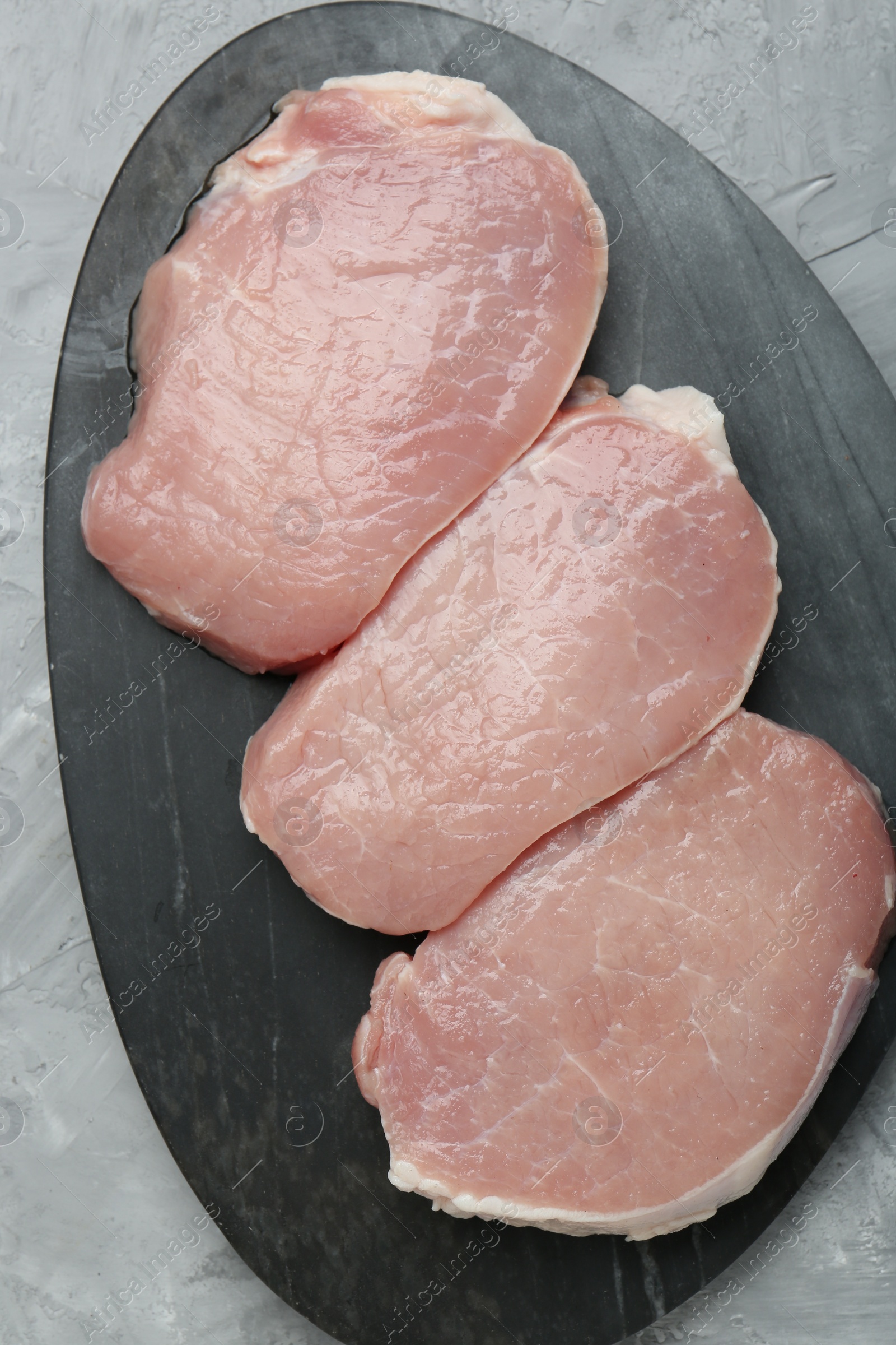 Photo of Pieces of raw pork meat on grey textured table, top view