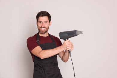 Smiling hairdresser with dryer on light grey background