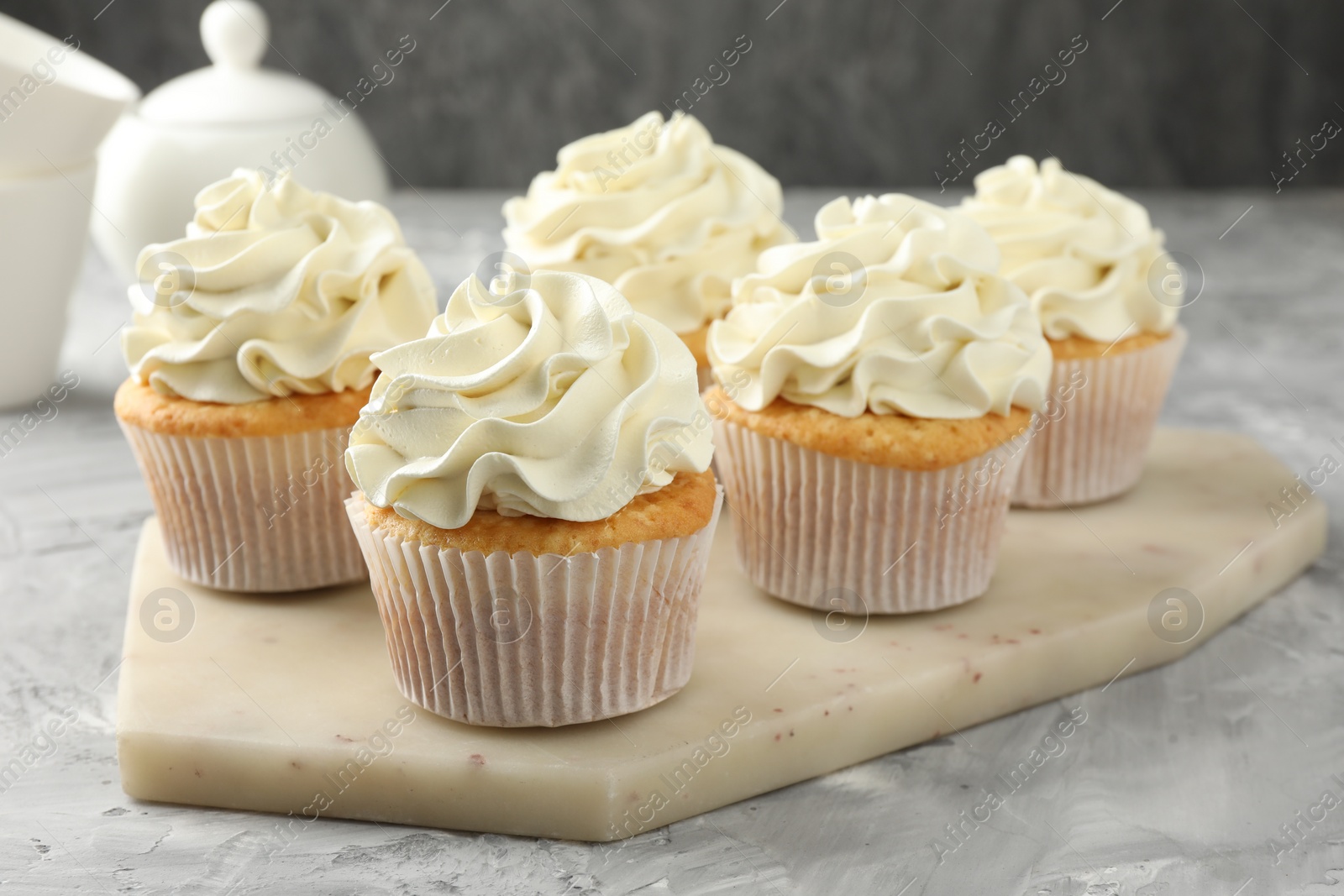 Photo of Tasty cupcakes with vanilla cream on grey table, closeup