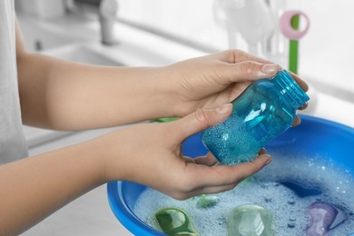 Photo of Woman holding baby bottle above basin with water in kitchen, closeup