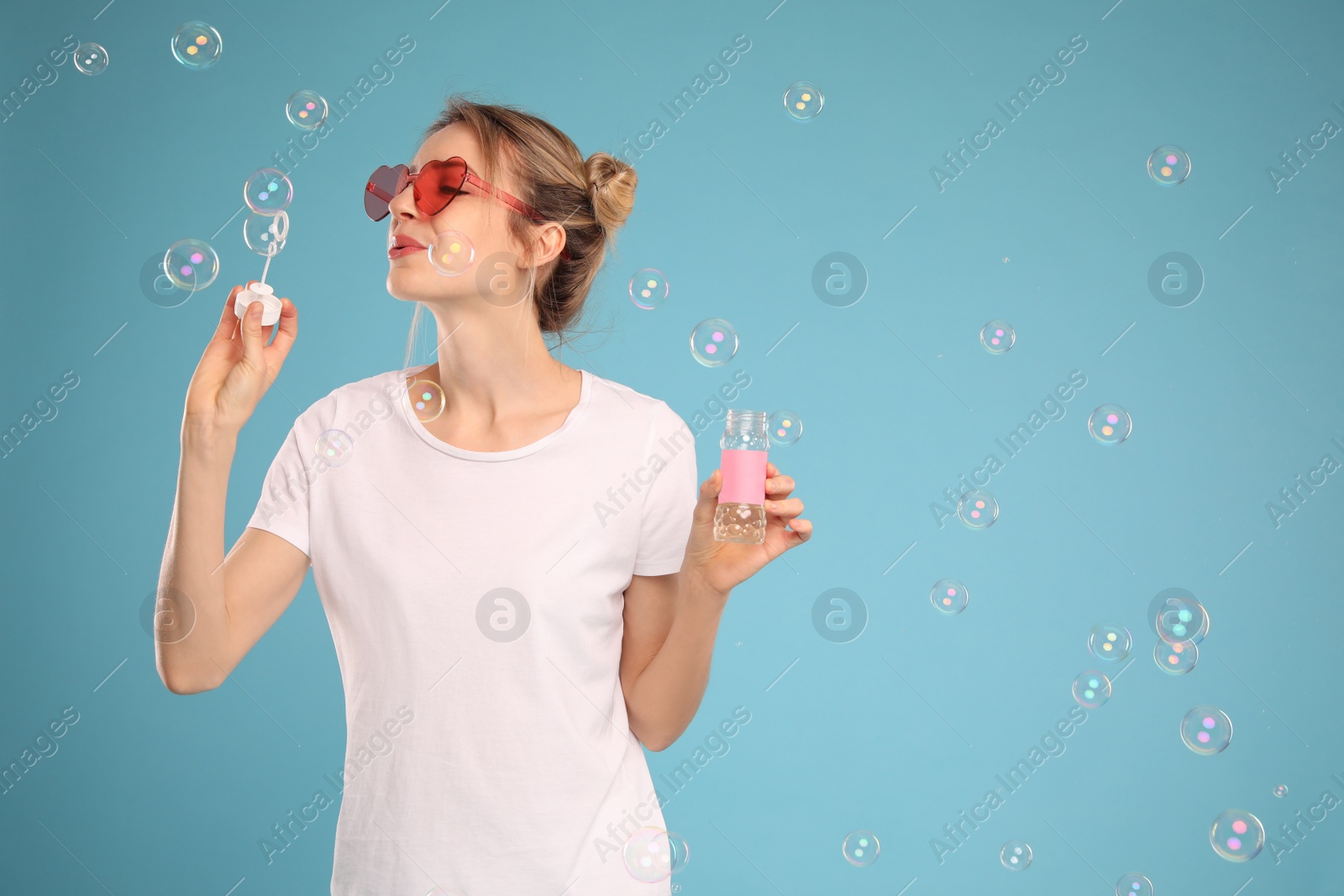 Photo of Young woman blowing soap bubbles on light blue background, space for text