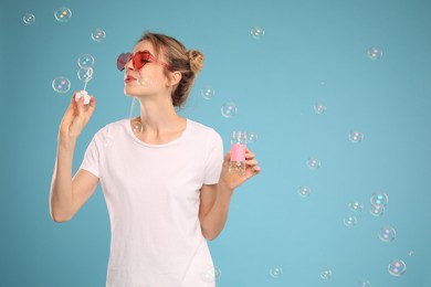 Young woman blowing soap bubbles on light blue background, space for text