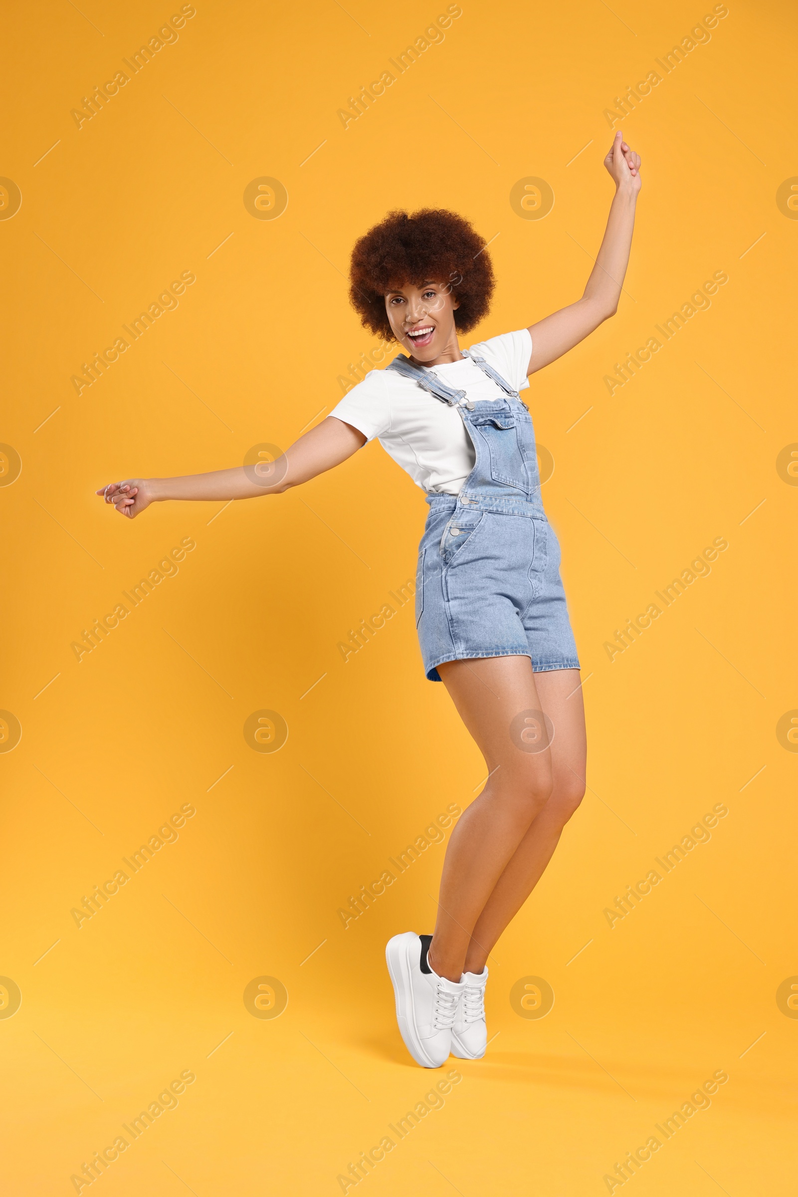 Photo of Happy young woman dancing on orange background