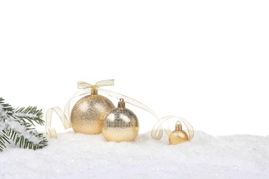 Beautiful golden Christmas balls with bow and fir tree branch on snow against white background