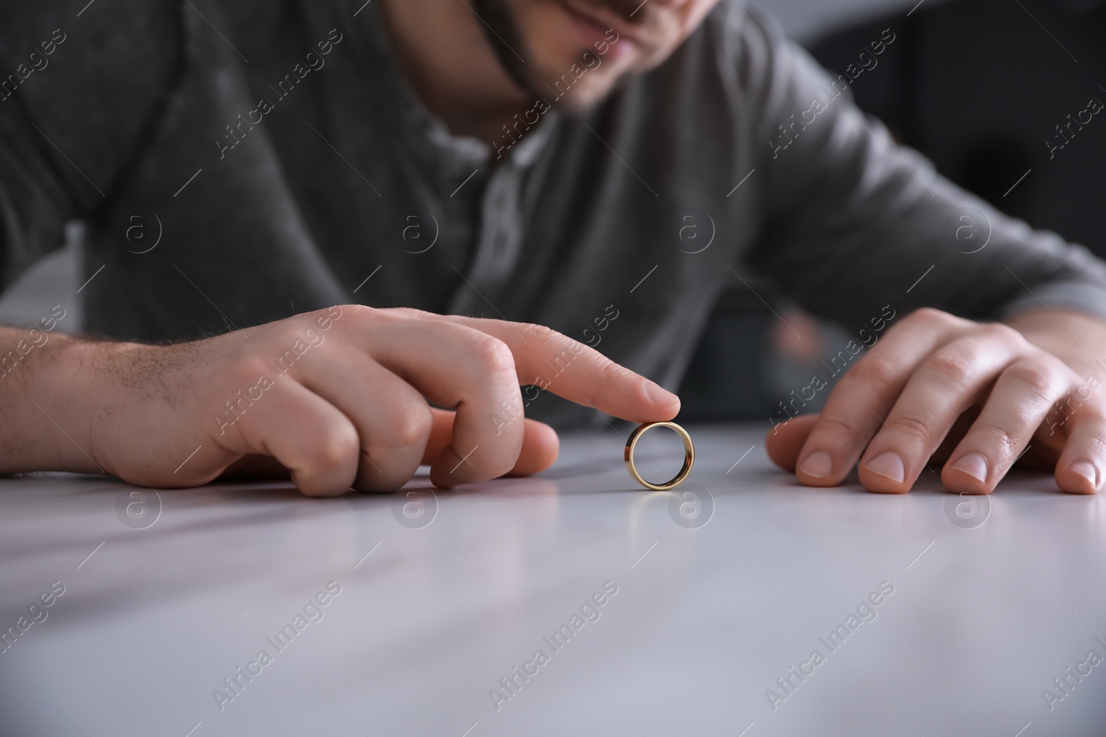 Photo of Man with wedding ring at white table, closeup. Divorce concept