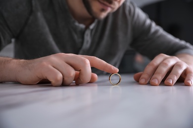 Photo of Man with wedding ring at white table, closeup. Divorce concept