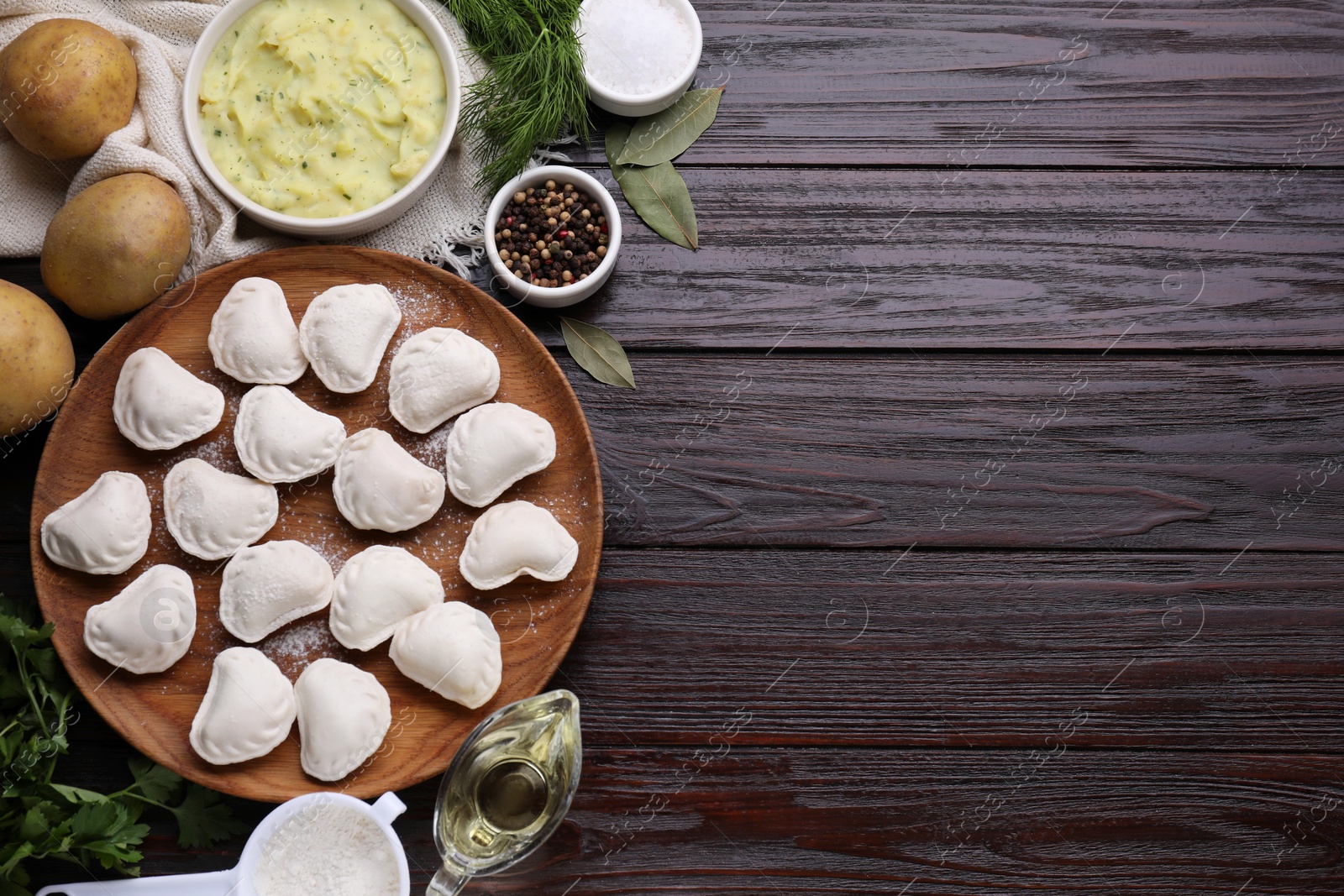 Photo of Raw dumplings (varenyky) and ingredients on brown wooden table, flat lay. Space for text