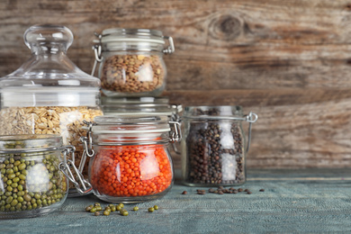 Photo of Different types of legumes and cereals in glass jars on blue wooden table, space for text. Organic grains