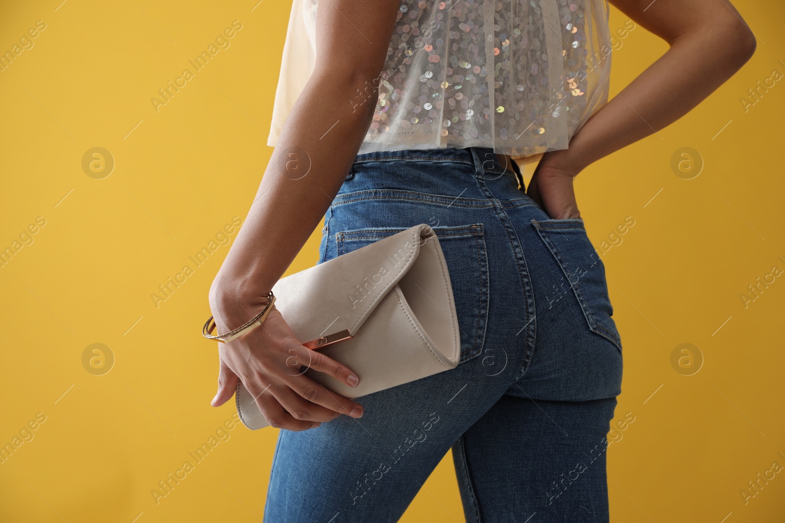 Photo of Woman in jeans with clutch purse on yellow background, closeup