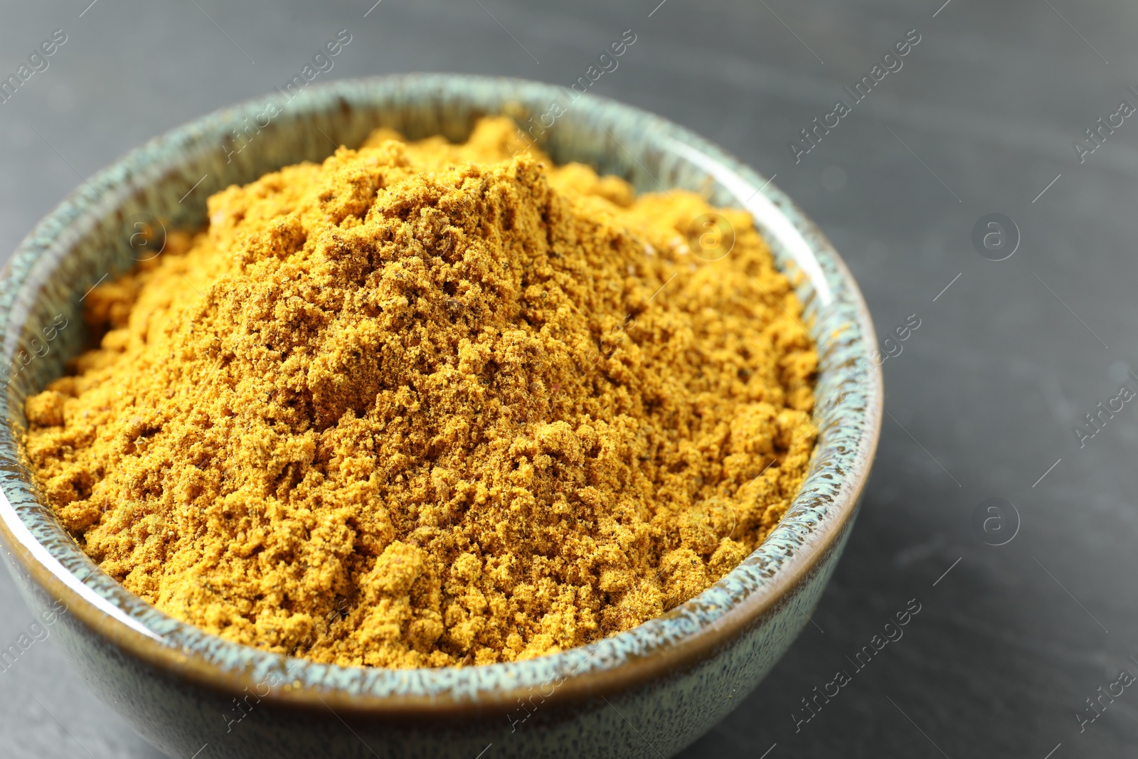 Photo of Dry curry powder in bowl on dark table, closeup