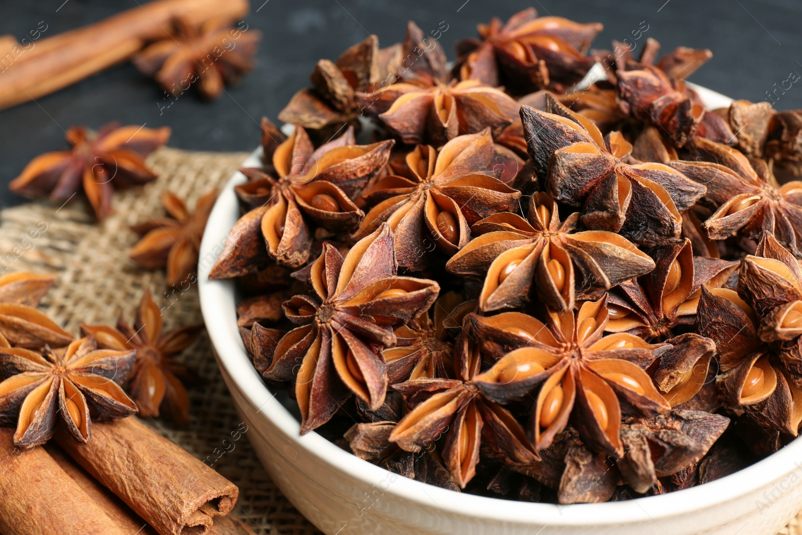 Photo of Bowl with aromatic anise stars and cinnamon sticks on table, closeup