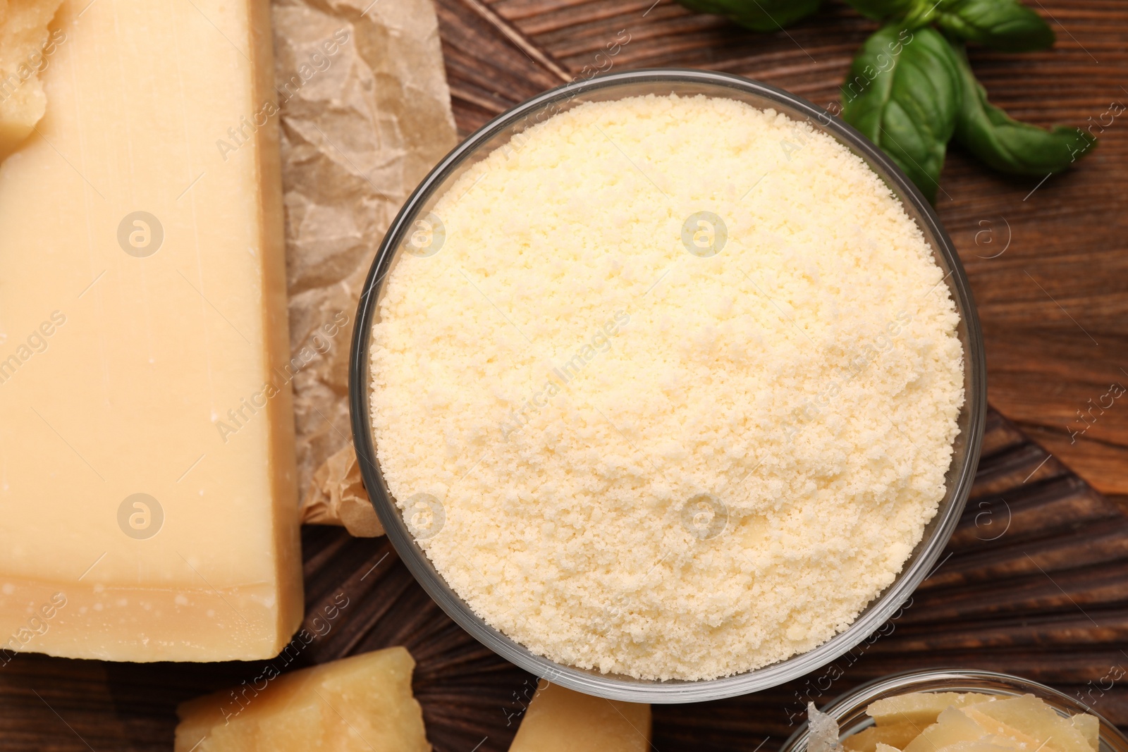 Photo of Delicious grated parmesan cheese in bowl on wooden table, flat lay