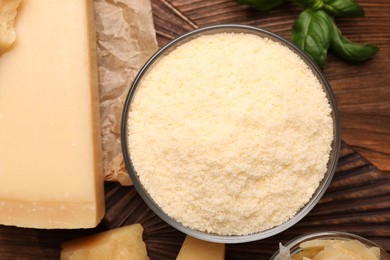 Photo of Delicious grated parmesan cheese in bowl on wooden table, flat lay