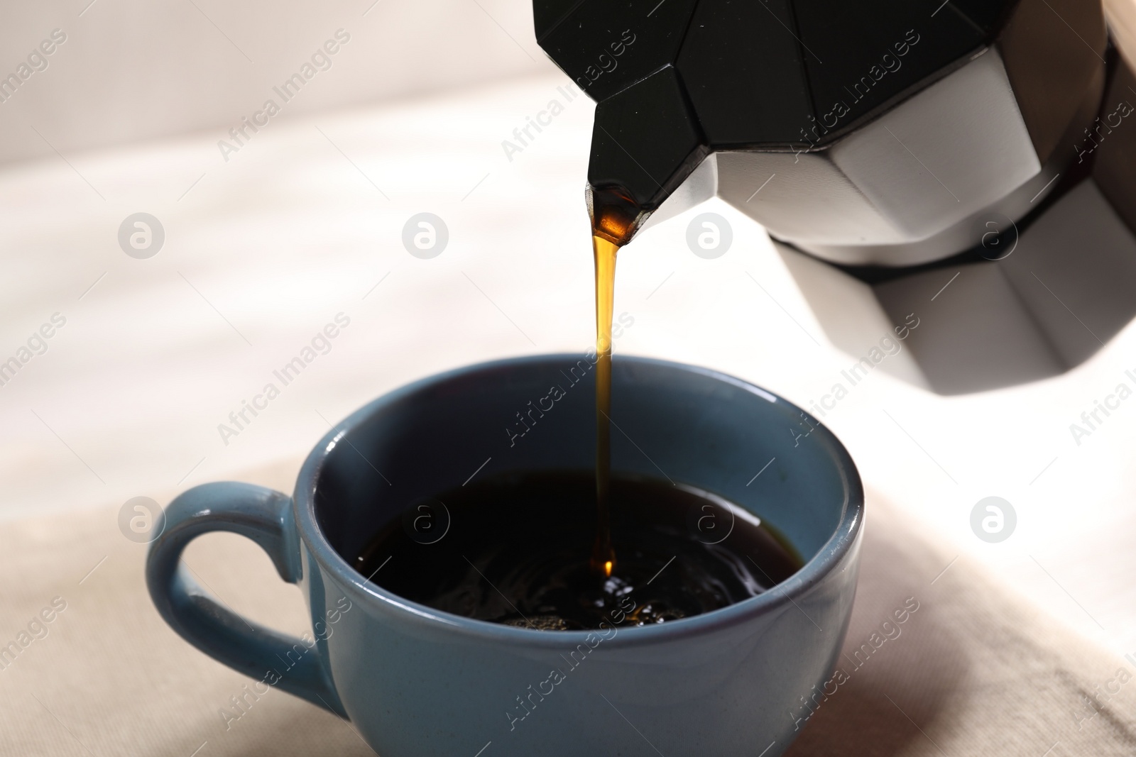 Photo of Pouring aromatic coffee from moka pot into cup at white table, closeup