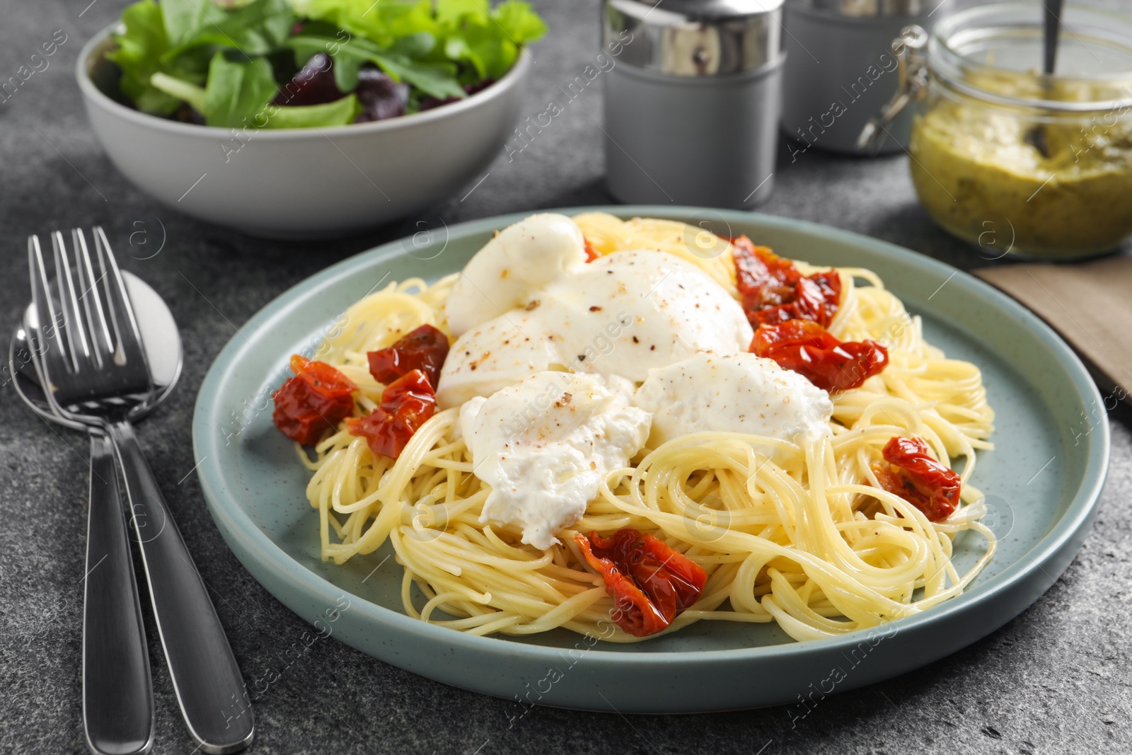 Photo of Delicious spaghetti with burrata cheese and sun dried tomatoes on grey table