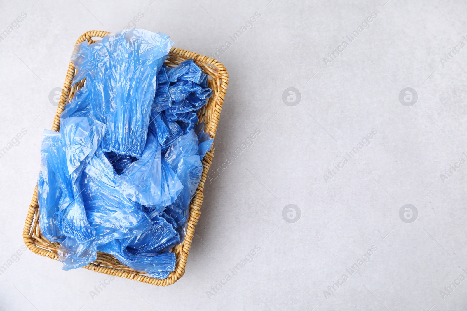 Photo of Blue medical shoe covers in wicker basket on light background, top view. Space for text