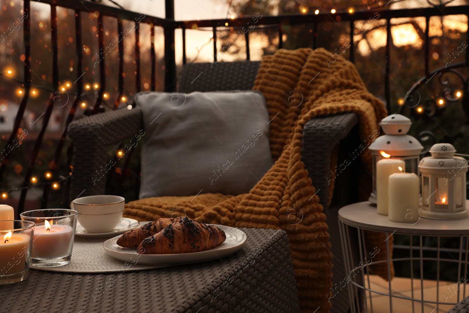 Photo of Beautiful view of garden furniture with pillow, soft blanket and burning candles at balcony