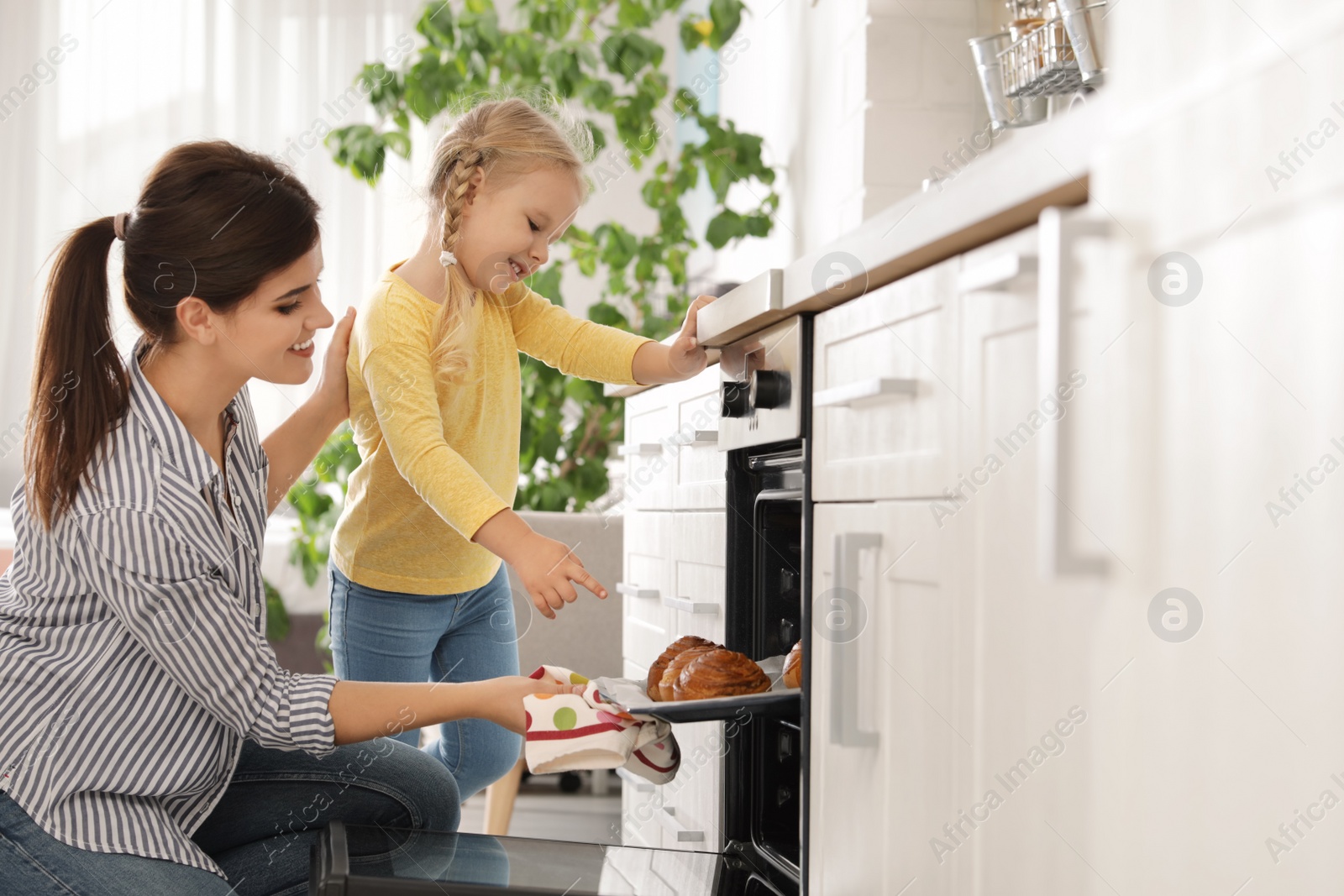 Photo of Mother and daughter taking out buns from oven in kitchen