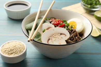 Photo of Tasty buckwheat noodles (soba) with chili pepper, egg, mushrooms and chopsticks on light blue wooden table, closeup