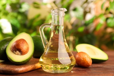Photo of Fresh avocados and jugcooking oil on wooden table against blurred green background, closeup