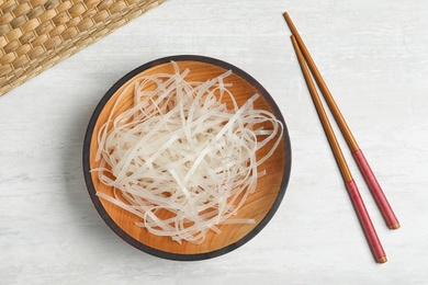 Plate of uncooked rice noodles and chopsticks on light table, flat lay