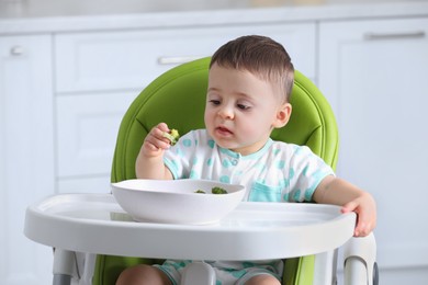 Photo of Cute little baby eating healthy food in high chair at home