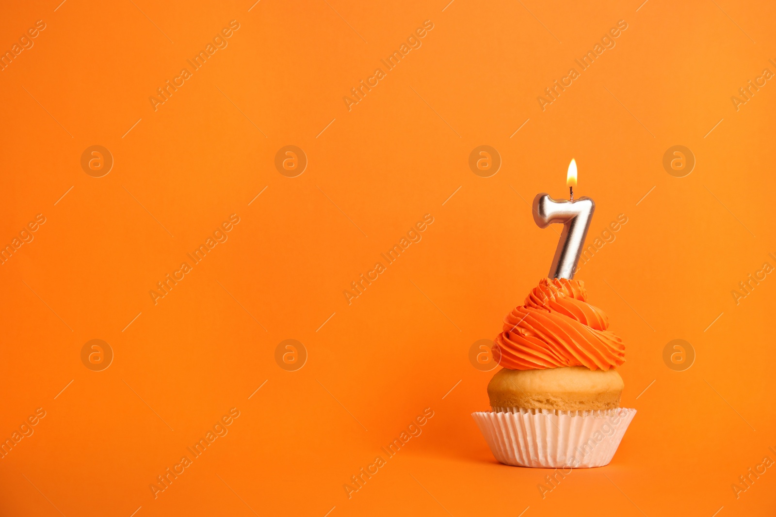 Photo of Birthday cupcake with number seven candle on orange background, space for text