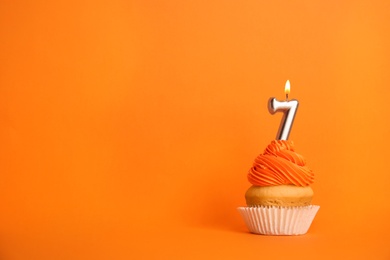 Photo of Birthday cupcake with number seven candle on orange background, space for text