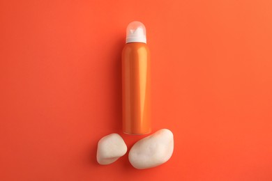 Bottle of sunscreen and stones on coral background, flat lay