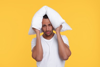 Photo of Tired man covering ears with pillow on orange background. Insomnia problem