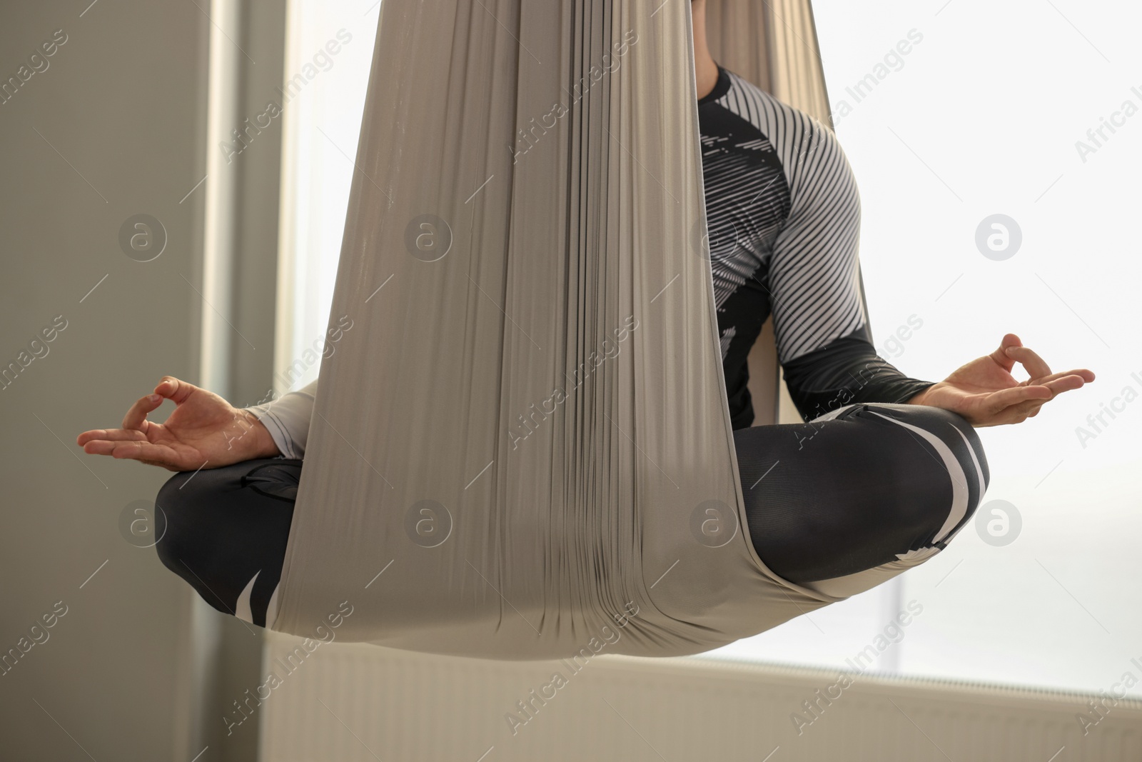 Photo of Man meditating in fly yoga hammock indoors, closeup