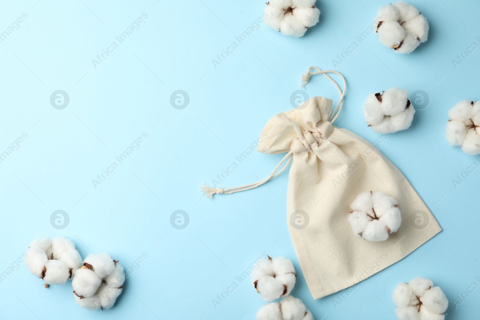 Photo of Cotton eco bag and flowers on light blue background, flat lay. Space for text