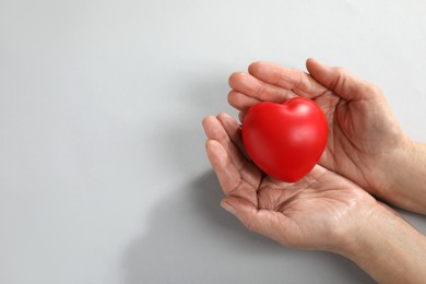 Photo of Elderly woman holding red heart in hands on light grey background, top view. Space for text