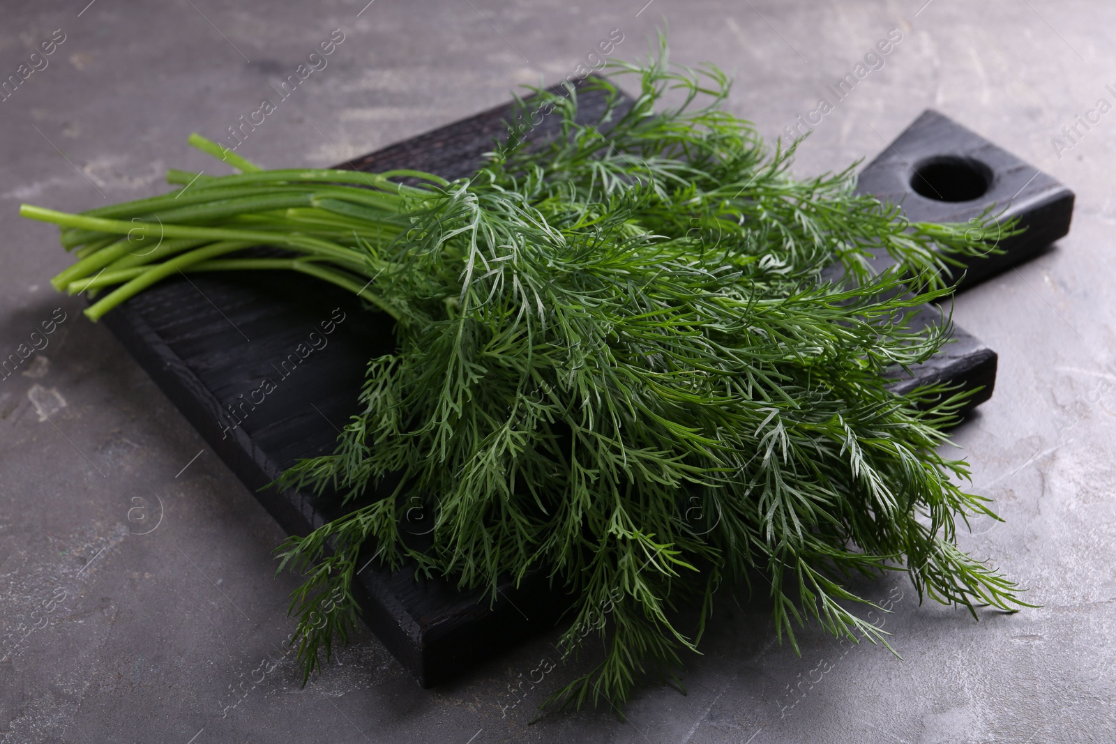 Photo of Board with sprigs of fresh dill on grey textured table, closeup